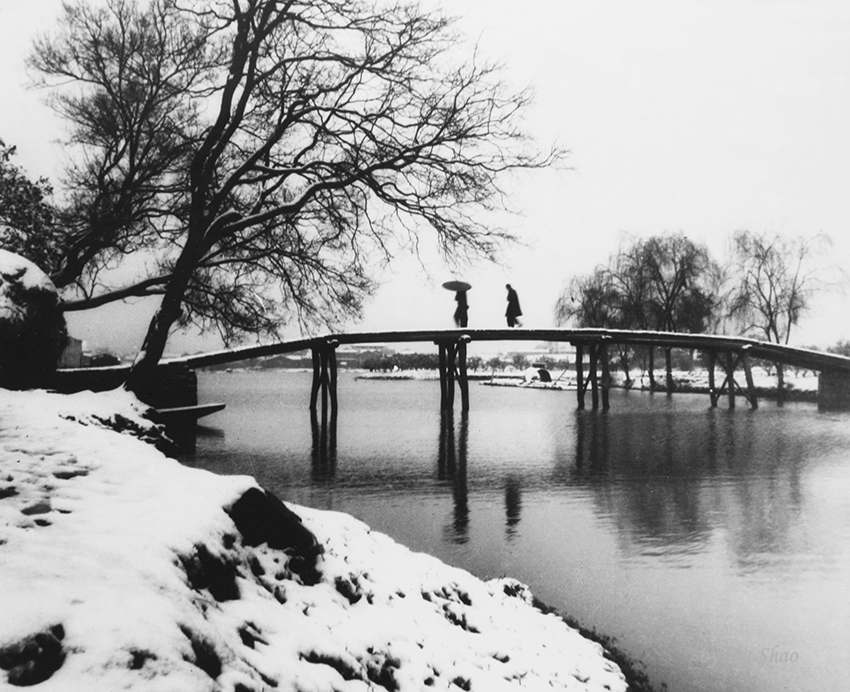 Two figures crossing a bridge during a snowy night